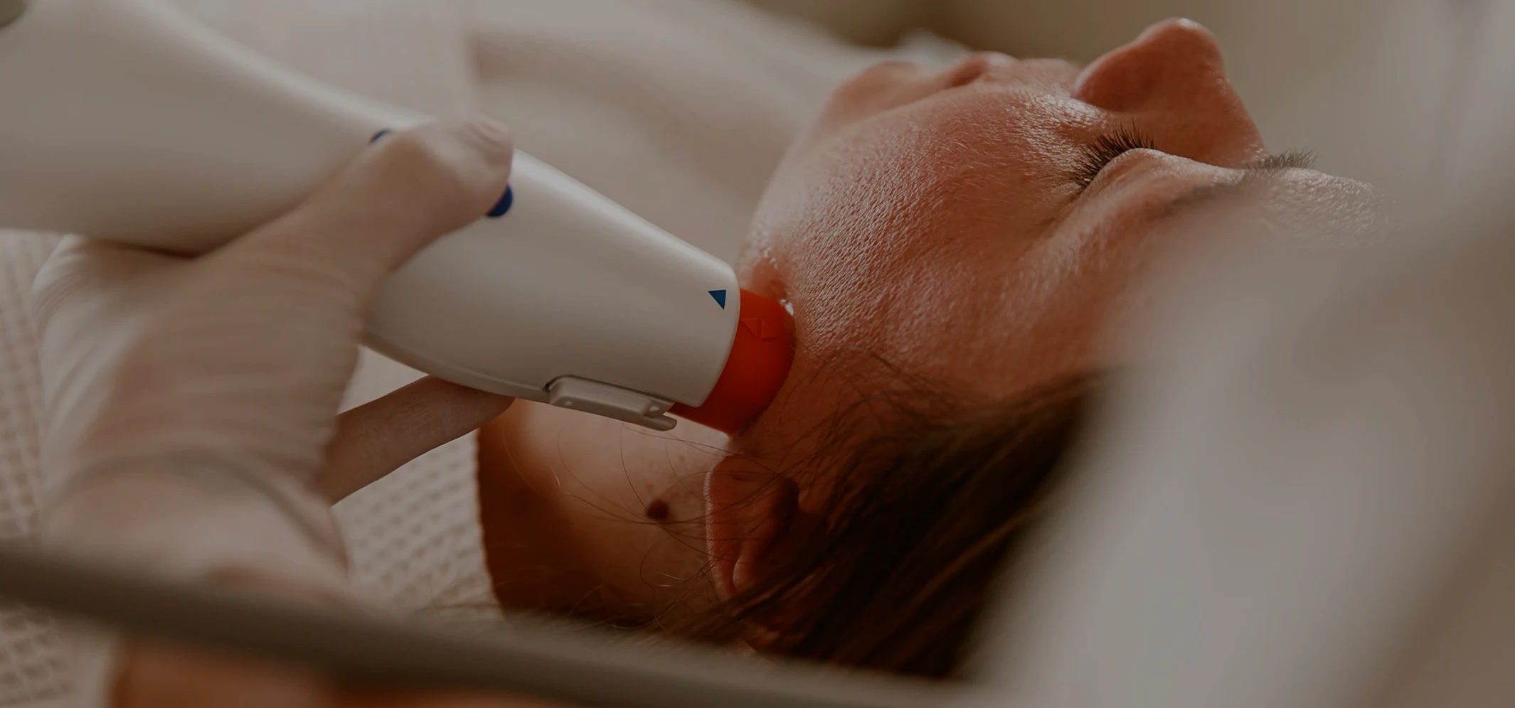 Close-up of a skincare professional wearing gloves performing a facial treatment with a handheld device on a woman's cheek.