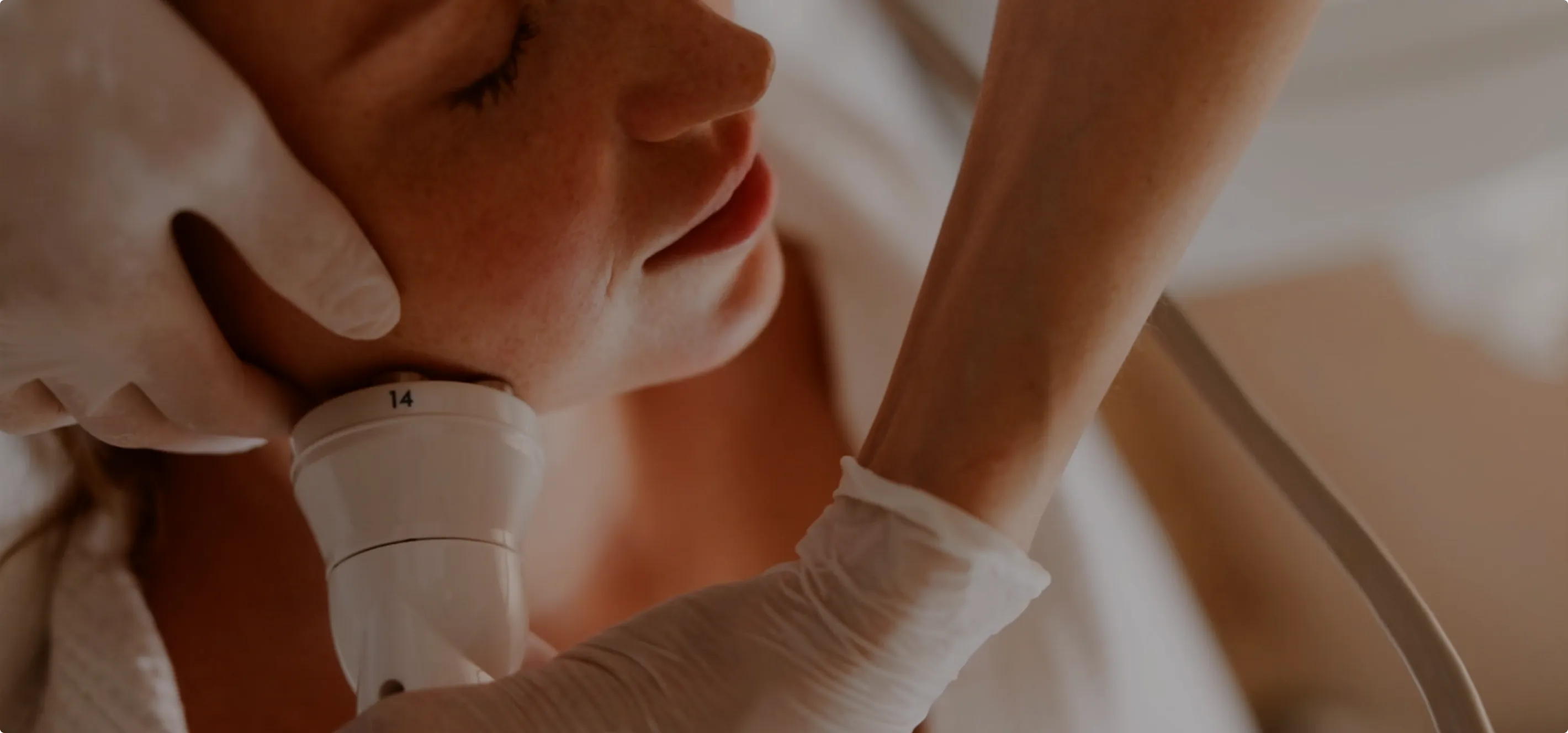 A close-up of a woman receiving an ultrasound neck examination by a gloved medical professional.