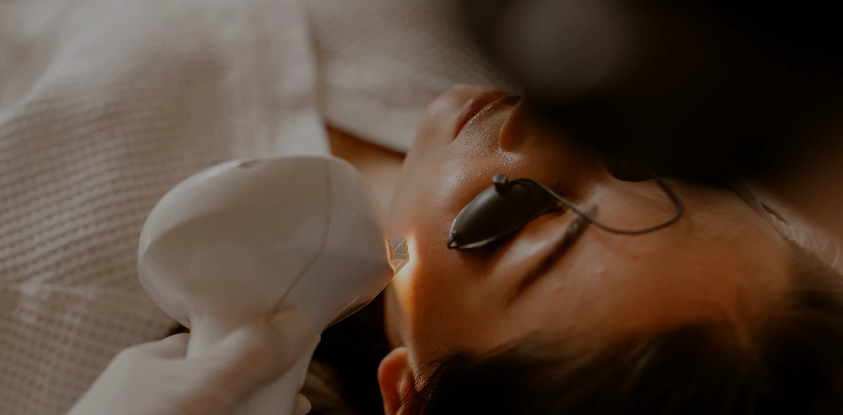 Close-up of a person wearing protective eye covers undergoing a laser facial treatment on the cheek.