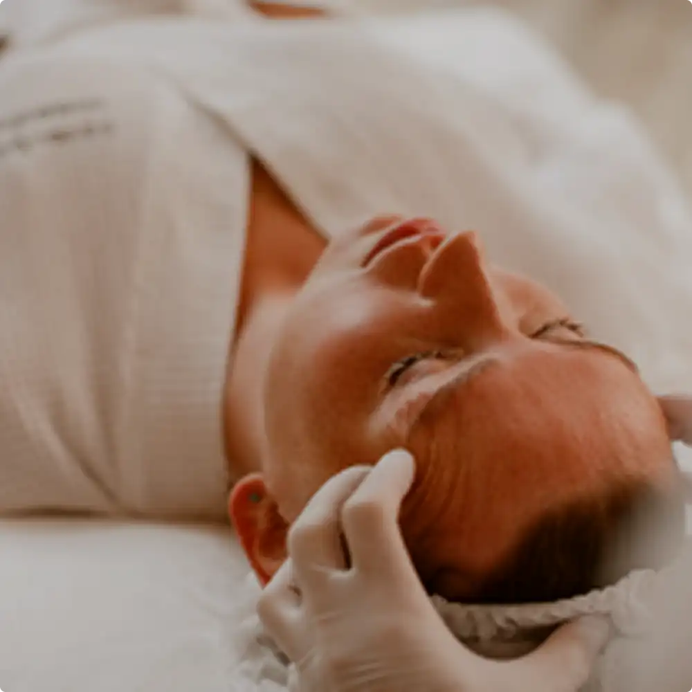 Close-up of a woman receiving a gentle facial massage, lying down with eyes closed and wearing a headband.