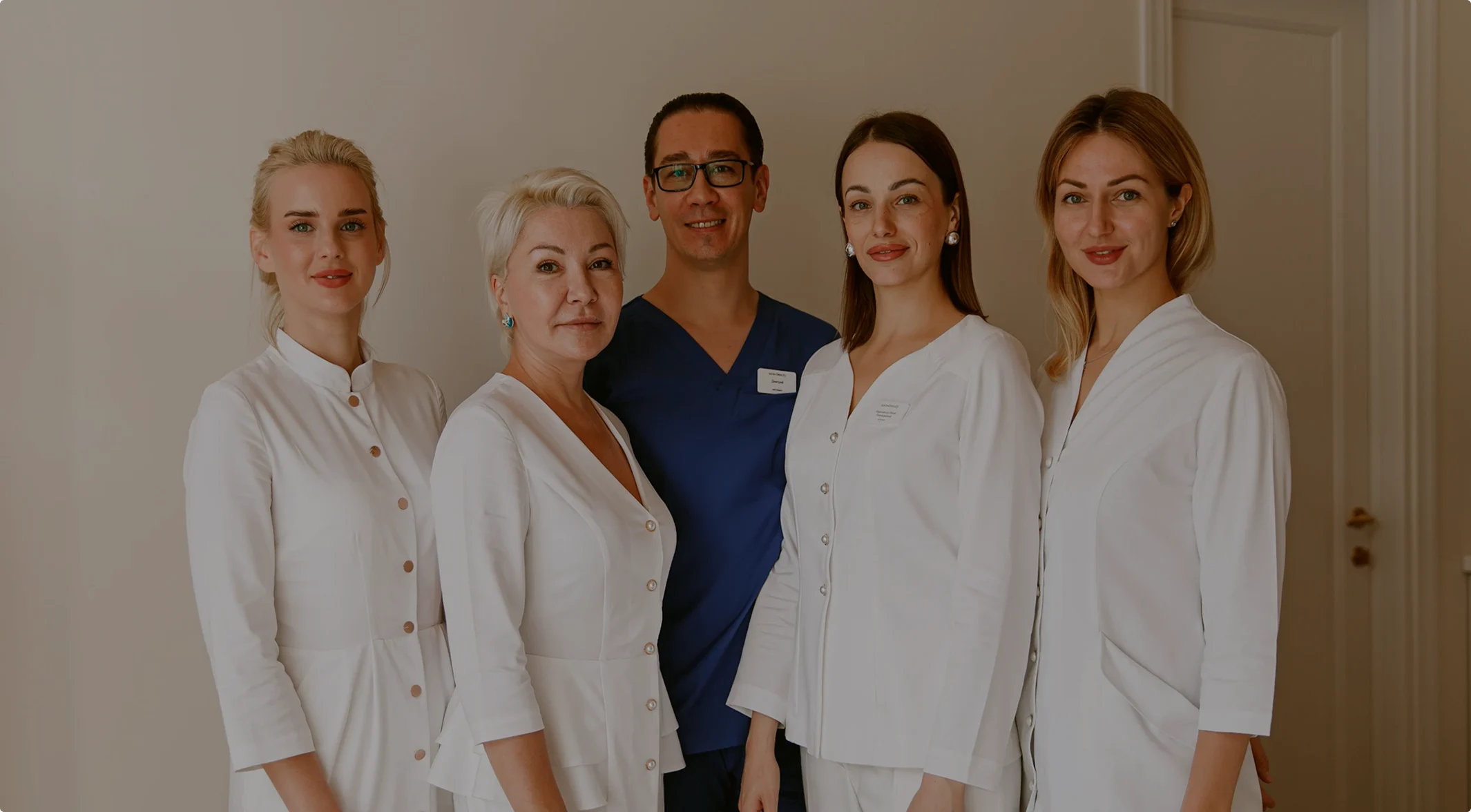 Group of five medical professionals in white and navy uniforms smiling indoors.
